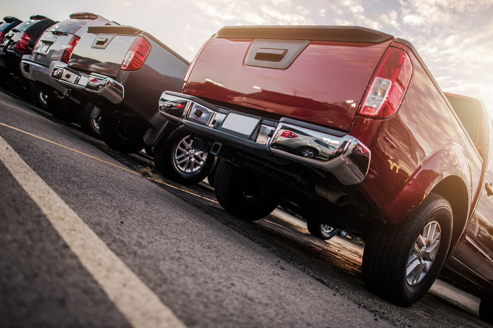 Row of SUVs and trucks parked at sunset, red SUV in the foreground, sun flaring off the chrome.